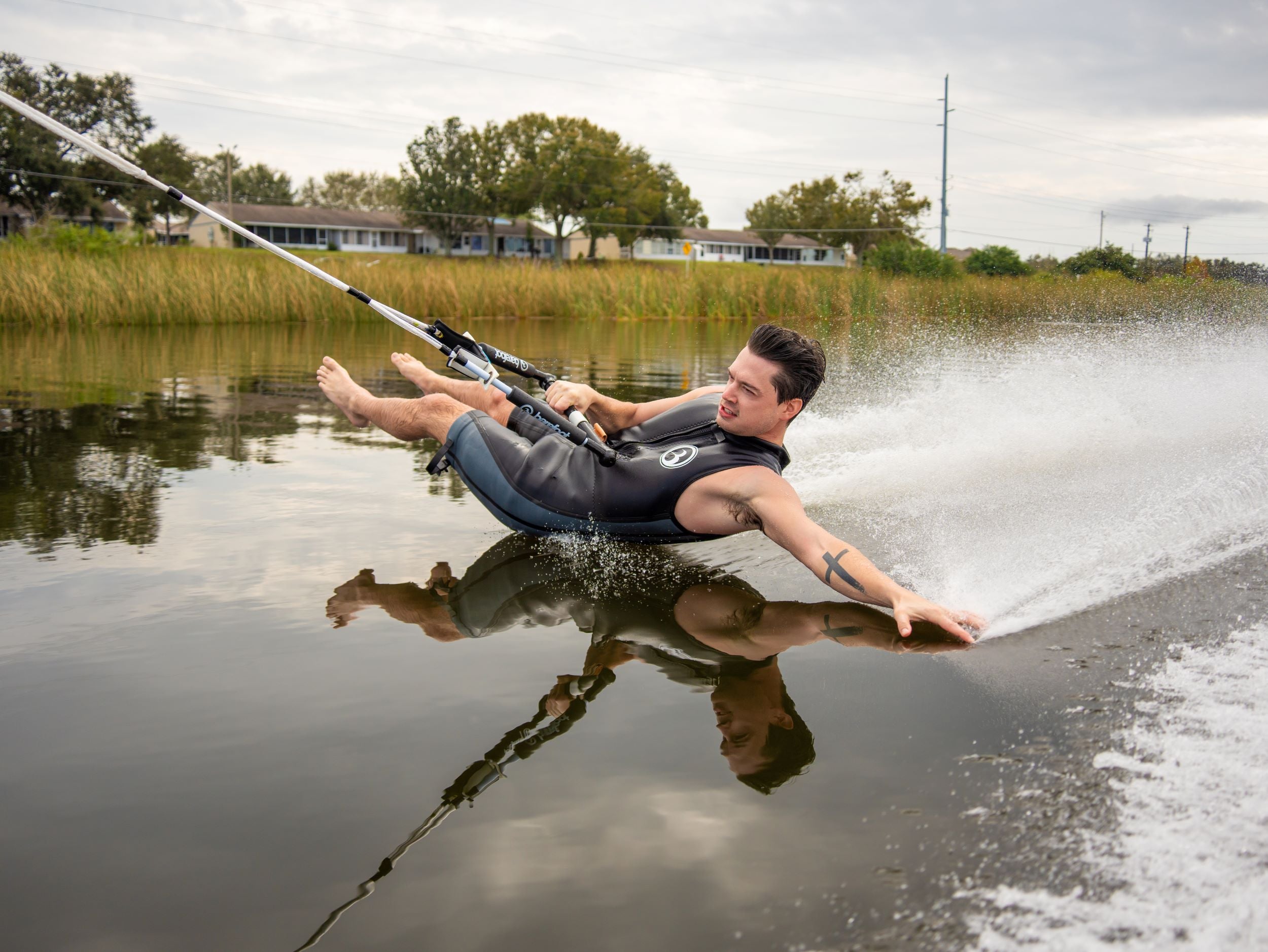 Barefoot waterskier gliding across the water with a boom, leaning back as water sprays around him.